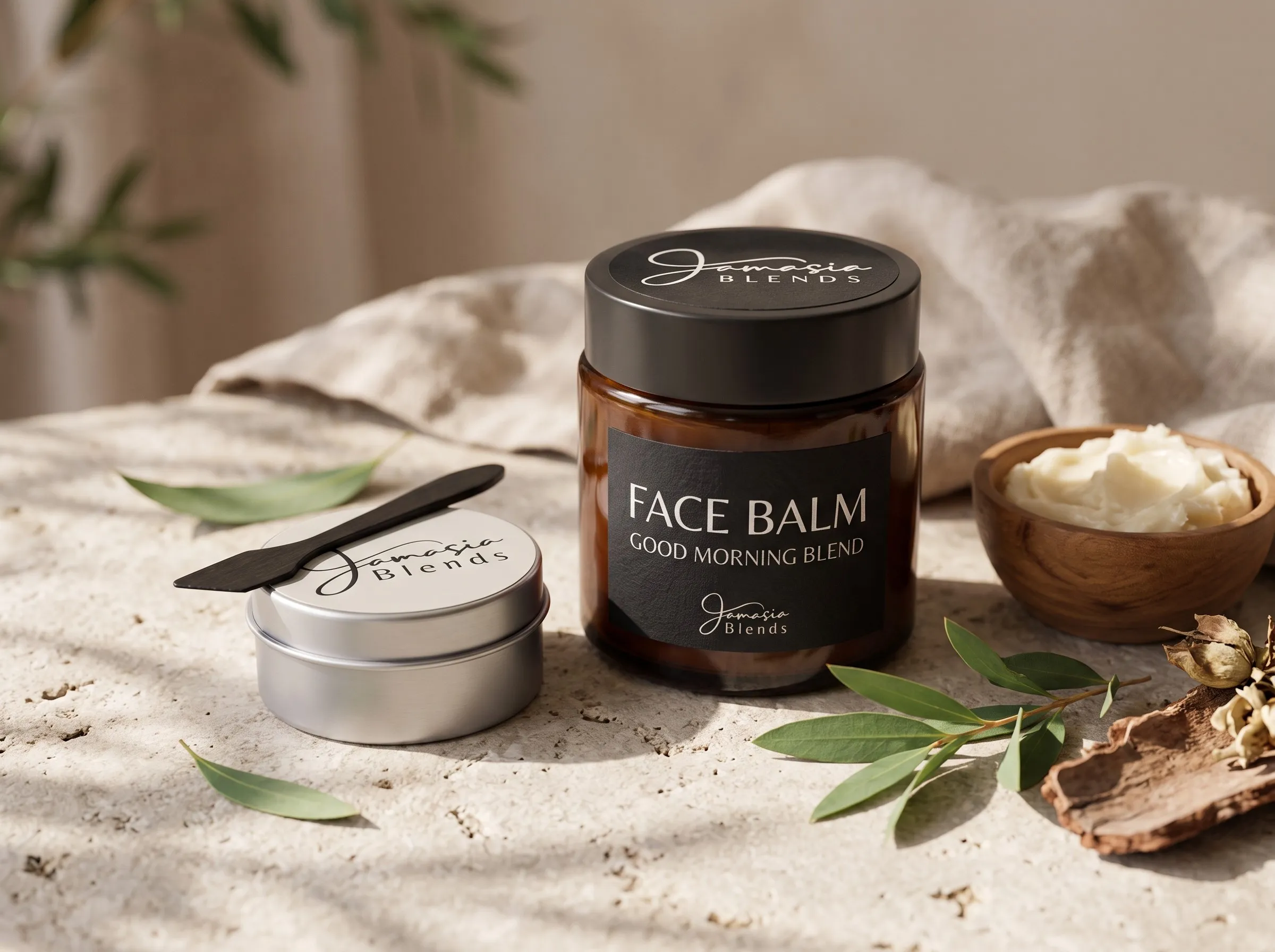 Jamasia Blends Face Balm in an amber jar beside a travel tin, with olive leaves and a wooden bowl of balm